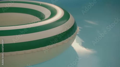 Green and white striped inflatable swim ring floating in swimming pool water. Summer recreation video. Poolside leisure and vacation concept.
