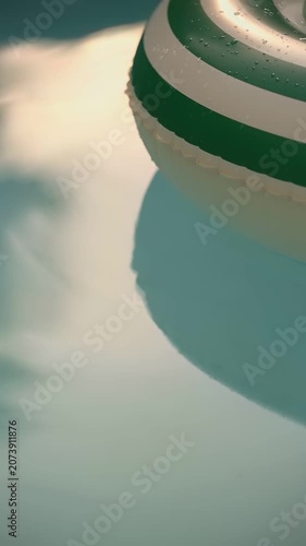 Striped Inflatable Ring Floating on Turquoise Swimming Pool Water in Summer. Close-up shot of a green and white striped inflatable swim ring floating on the surface of a clear turquoise swimming pool.