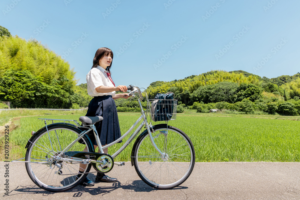 Obraz premium 田園風景の中で自転車と立つ女子高校生の通学風景