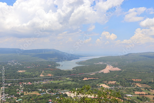 panoramic view of mountains, winding reservoir, lush forests, beautiful clouds, and picturesque countryside under clear blue sky, in Thailand