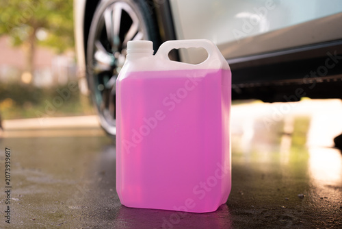 Cuadro en lienzo Plastic canister with pink liquid stands on wet ground near car wheel close up