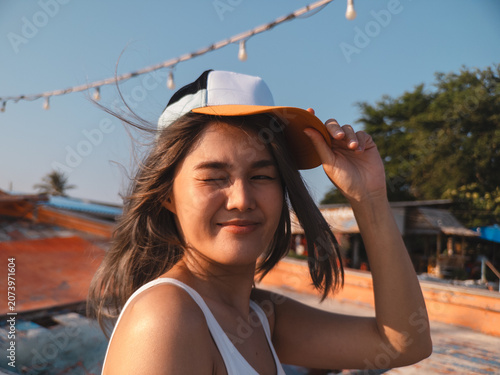 Cheerful Asian woman in casual attire capturing sunny marina memories