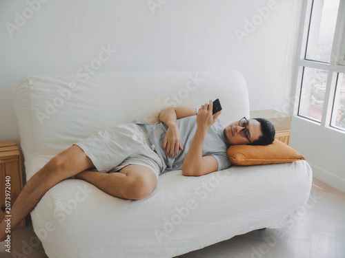 Asian man focus on the phone while relaxed on the sofa.