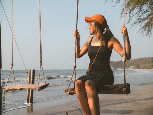 Female relaxing on beach swing with boats nearby and waves