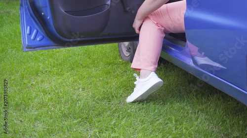 Woman stepping out of blue car onto green grass, A woman in pink pants gets out of a car onto a green lawn