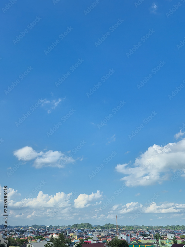 Obraz premium Blue sky with white clouds over small city landscape and green hills during daytime