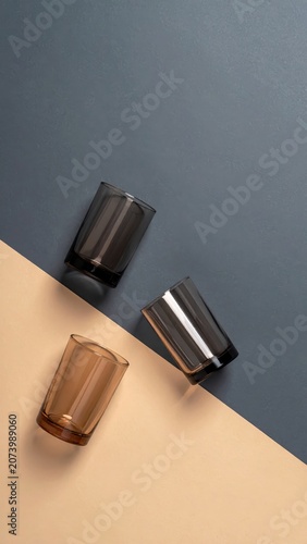 Three colored glass tumblers arranged artistically on a split background of taupe and dark gray.