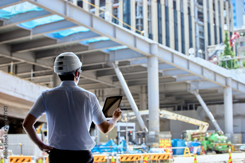 Obraz w ramie 都市開発の建設現場でタブレットを操作して工事の監理業務を行うヘルメットを被った男性の技術者