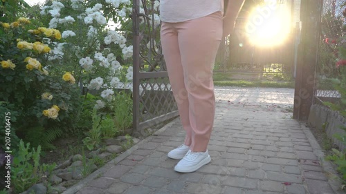 Woman near a rose bush at sunset, Woman in pink pants standing near blooming rose bush in garden at sunset