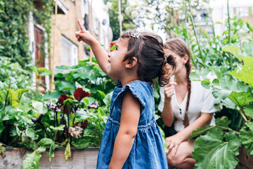 Daughter pointing while standing with mother in background at vegetable garden