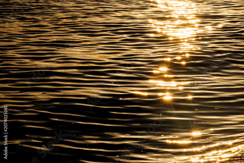 Fotografie Horizontal abstract view of sparkling golden sunset reflections on dark ocean ripples