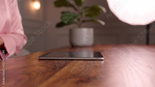 A close-up of a stylish wooden table featuring a tablet and a leafy plant, showcasing a serene indoor environment with soft lighting in the background