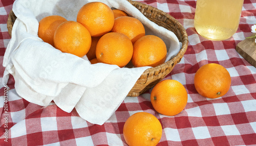 photograph of a group of oranges in a basket with a white cloth under them. Some of the oranges are spilled out onto a picnic blanket