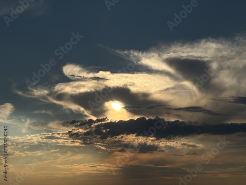 Dramatic sunset sky with glowing sun behind dark clouds and atmospheric clouds