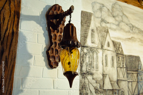 an elegant vintage wall lantern lamp made of carved oak wood with yellow amber glass hanging on a white brick wall