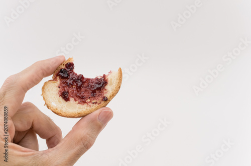 Primo piano di mano che regge una fetta di pane addentata con marmellata su uno sfondo bianco