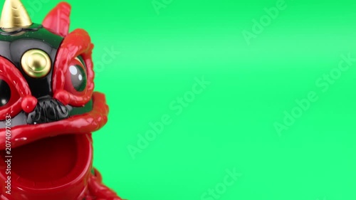 Close-up studio shot of a Chinese lion dance toy nodding. The camera smoothly pans right to reveal a blank green screen chroma key backdrop, perfect for adding text or custom video effects