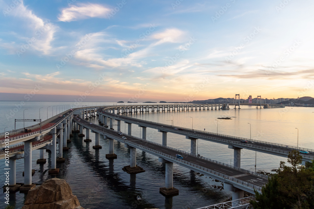 Fototapeta premium Kuahai Bridge View Point, spectacular double-deck suspension bridge. Stunning panoramic views of the sea, making it one of Dalian's best places for sightseeing. Bridge curving over calm sea at sunset.