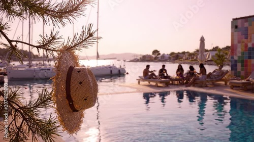 A Relaxing Summer Gathering by the Pool with a Hat Hanging from a Tree and Friends Enjoying a Beautiful Sunset by the Marina
