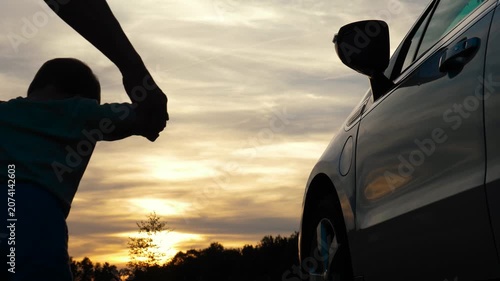 Silhouette of loving parent holding hands with little child playfully interacting with a car, capturing pure curiosity and a spirit of adventure against a sunset backdrop