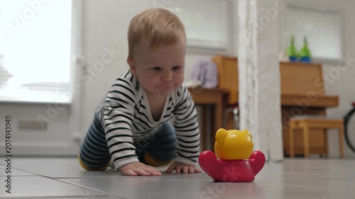 Infant moves toward bright colorful toy. Child crawling across room to grasp vibrant toy with enthusiasm. Young child carefully navigates floor aiming to grasp brightly colored plaything
