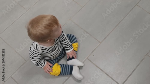 Young child observes with curiosity indoors. Inquisitive toddler sitting peacefully on tiled floor. Child with light hair in quiet home environment, top view