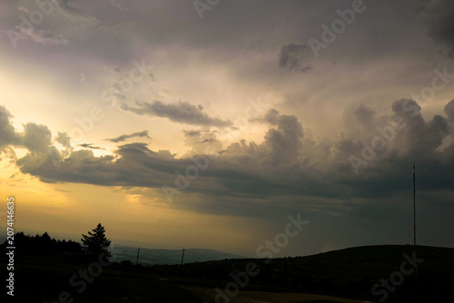 This dramatic scene depicts a stormy sunset with clouds breaking to reveal golden light.

The atmosphere resembles a rare optical weather phenomenon, where sunset colours glow behind dark storm clouds
