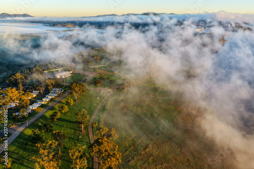 Quadro su tela Aerial view over the Lake Keepit campgrounds as fog drifts across the surrounding rural landscape beneath soft sunrise light in NSW, Australia