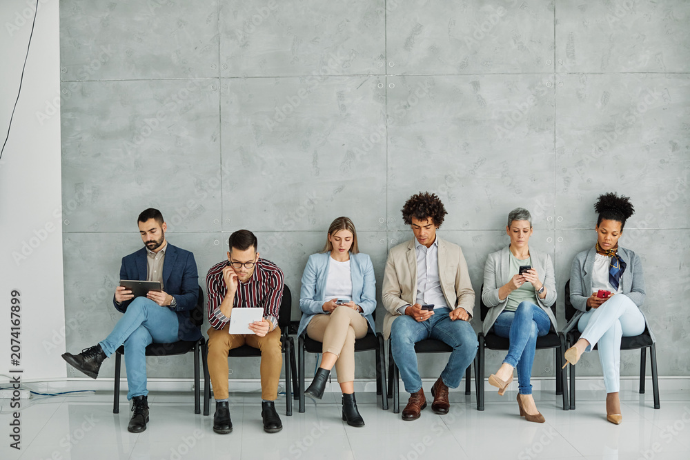 Fototapeta premium Portarit of a group of young business people using mobile phones waiting to apply for a job in the office