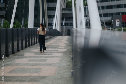 Bild auf Leinwand A businesswoman walks away along a modern pedestrian bridge in a city office district