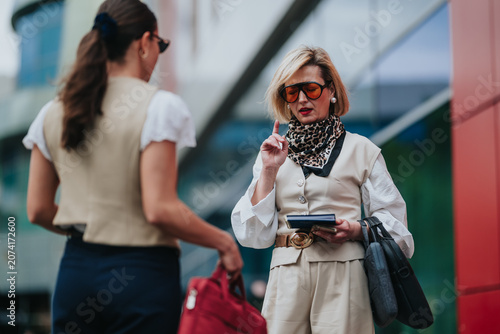Photos Two businesswomen stand outside a contemporary building as one reviews travel documents and a phone