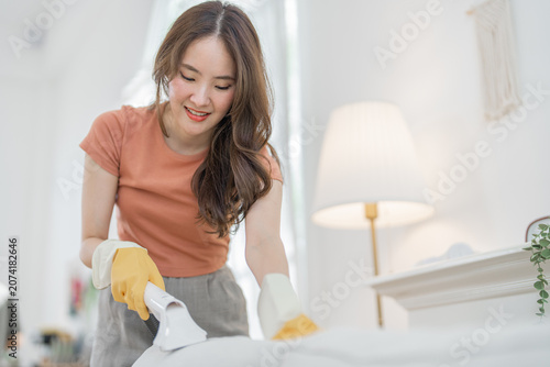 Woman cleaning spray glove home smile cloth room hygiene housework Asian woman smiling while cleaning fabric surface with spray bottle and gloves in bright home interior