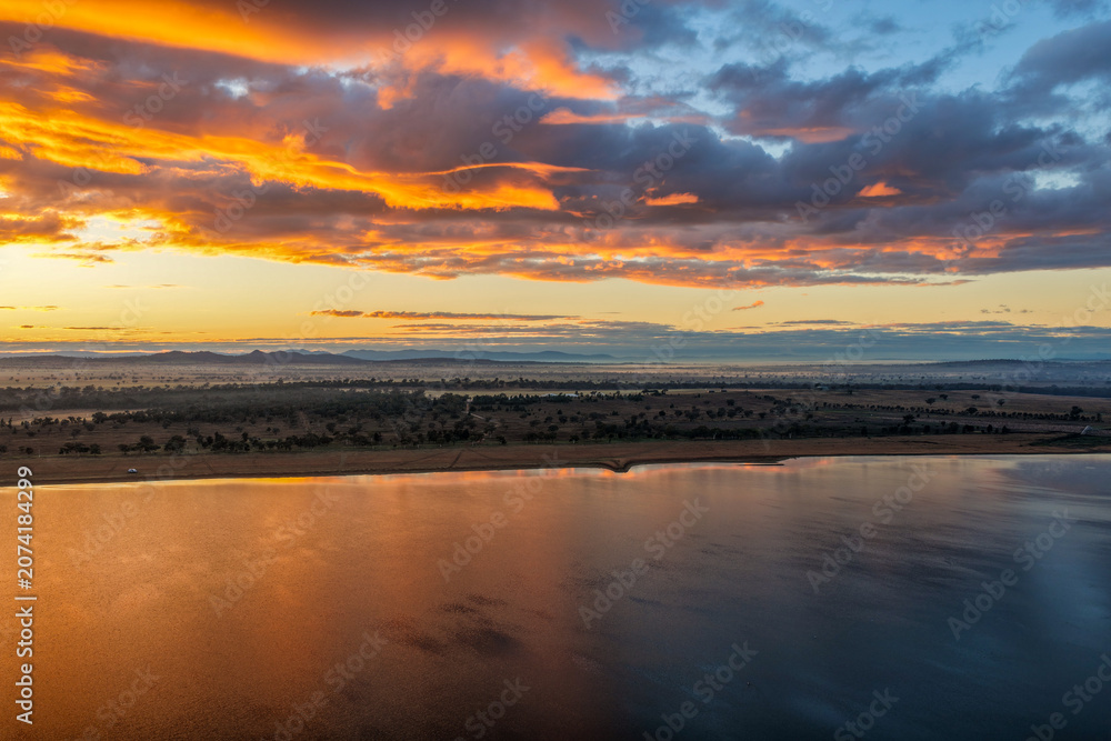 Fototapeta premium Aerial scene capturing a golden sunrise over Lake Keepit, with morning fog drifting across the surrounding rural landscape to create a peaceful and atmospheric setting in NSW, Australia.