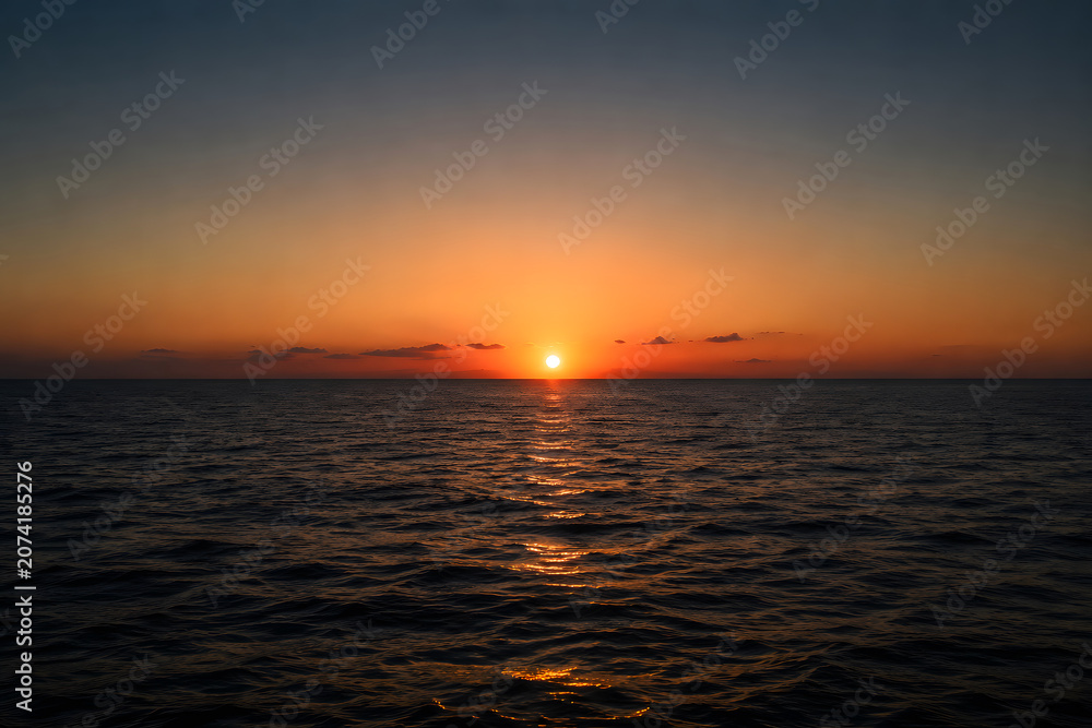 Fototapeta premium Beautiful sunset over calm ocean water with orange sky and clouds serene natural scene
