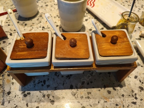 Condiment set with wooden lids and ceramic spoons on a speckled table