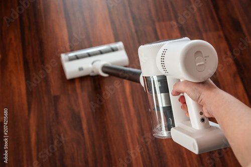 Fotografie First-person perspective (POV) of a woman using a powerful white cordless vacuum cleaner on a dark hardwood floor, ergonomic design for effortless home hygiene and spotless surface