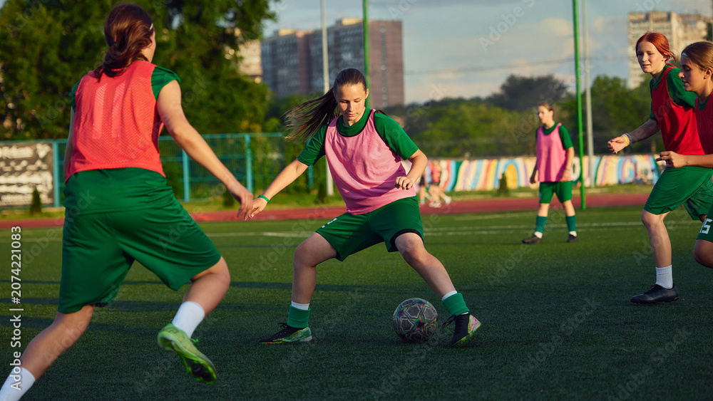 Fototapeta premium Teenage female soccer player dribbling ball during team football practice. Concept of ball control, small sided games, youth academy training and player development.