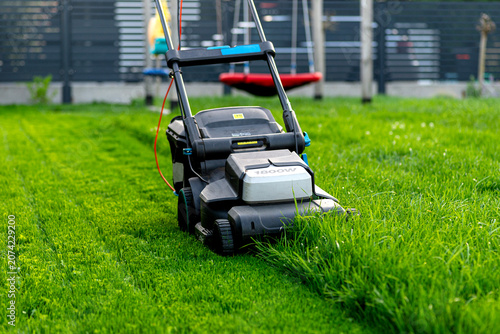 Electric lawn mower cutting overgrown green grass lawn