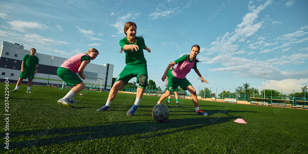 Obraz premium Girls soccer team dribbling ball during summer field practice. Concept of women football, match action, dribbling skills, teamwork, youth camp and sports advertising.