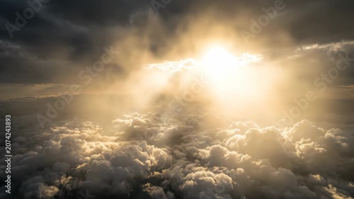 Aerial view of sun rays breaking through dramatic clouds over a sea of fluffy clouds. Heavenly nature, divine sunlight, and majestic weather phenomenon concept.