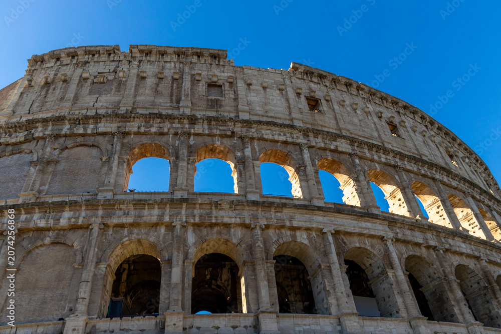 Obraz premium Famous Coliseum in Rome. Colosseum, or Coliseum. Part of the wall of an antique stone structure with arches. Italy, Europe. Famous touristic place in the world, Europe. Beautiful blue sky background.