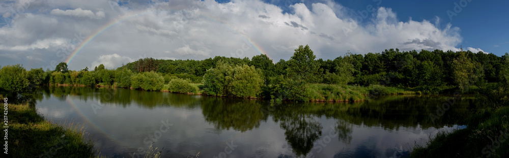 Fototapeta premium Panoramic landscape with rainbow reflected in a calm lake after rain