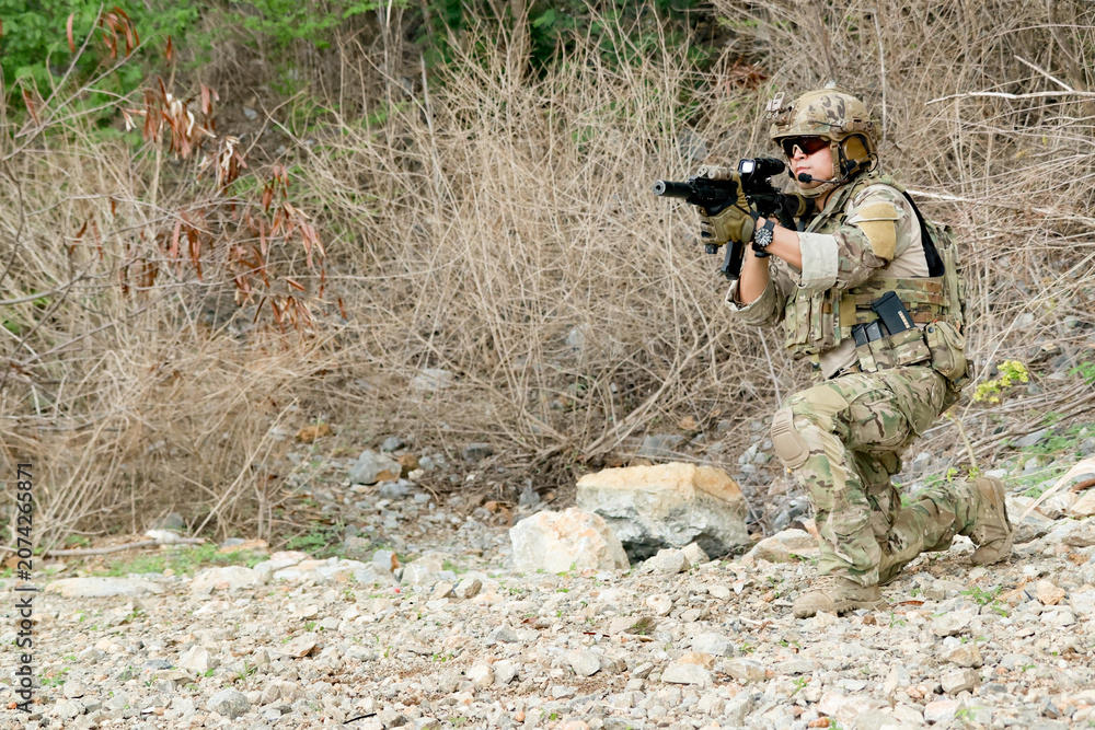 Fototapeta premium Soldiers prepare fire their guns at the enemy in front them ready attack stance : Soldiers wear camouflage uniforms in arid forest areas blend in with the wooded and mountainous terrain.