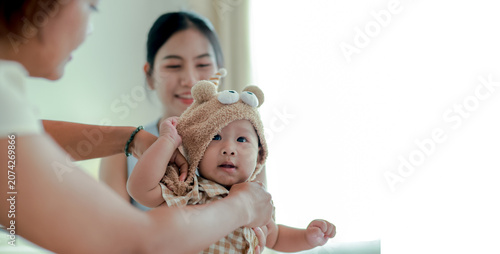 Εκτύπωση καμβά Mother gently and carefully places knitted hat on her adorable infant son while the nanny attentively assists in the warm embrace of their home moment of love care and bonding