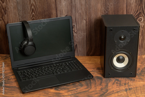 headphones hang on the laptop screen near the musical speaker