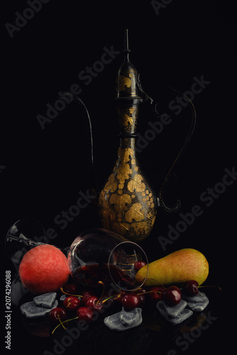 Still life. A beautiful pitcher, an overturned glass, a peach, and a pear against a dark background with a reflection.