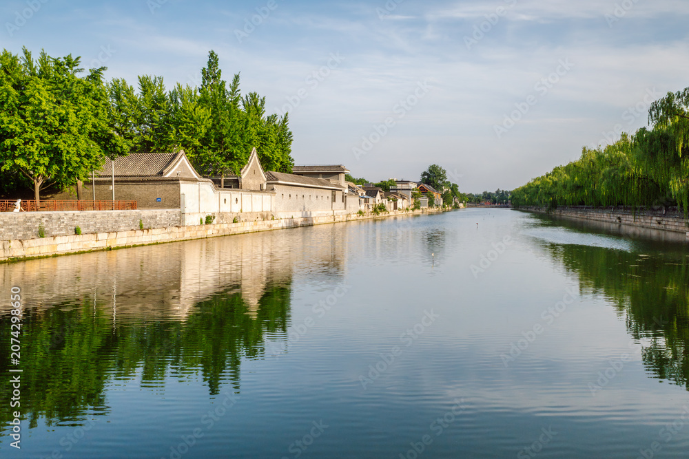 Fototapeta premium The moat surrounding the Forbidden City, known as the Tongzi River, in Beijing, China. It features the historic outer wall on the right side of the water. Traditional architecture along the banks.