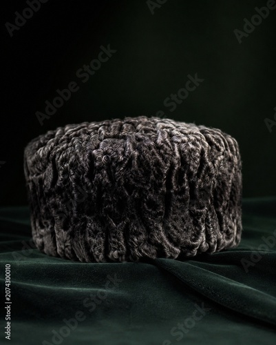 A Karakul fur hat resting on dark velvet, showcasing its texture.