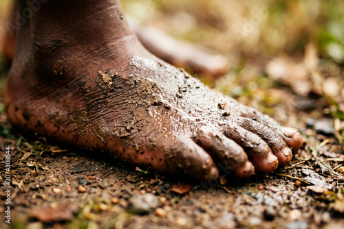 Close up of a bare foot covered in mud and dirt standing on the ground in nature