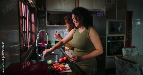 Fotografie Mother slicing vegetables while teenage daughter assists in kitchen, engaged in